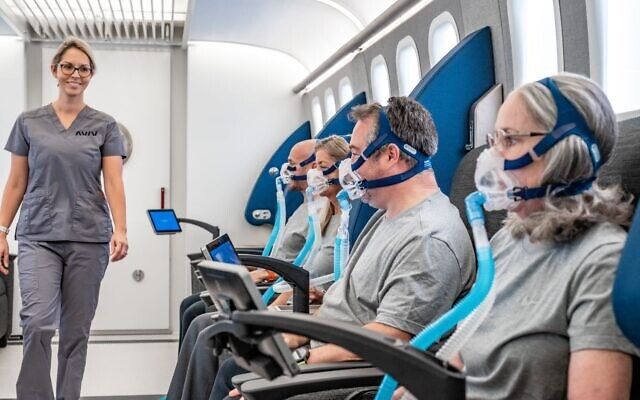 A group of people wearing masks are sitting on a plane.