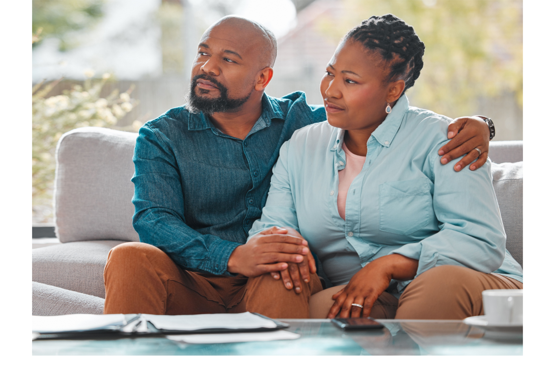Man with arm around woman, both looking off to the side, seated on a couch indoors.