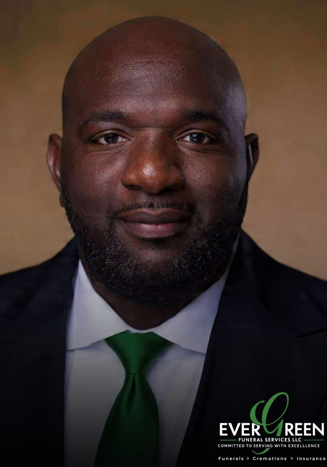 Man in suit, smiling, with a black tie against a tan background.