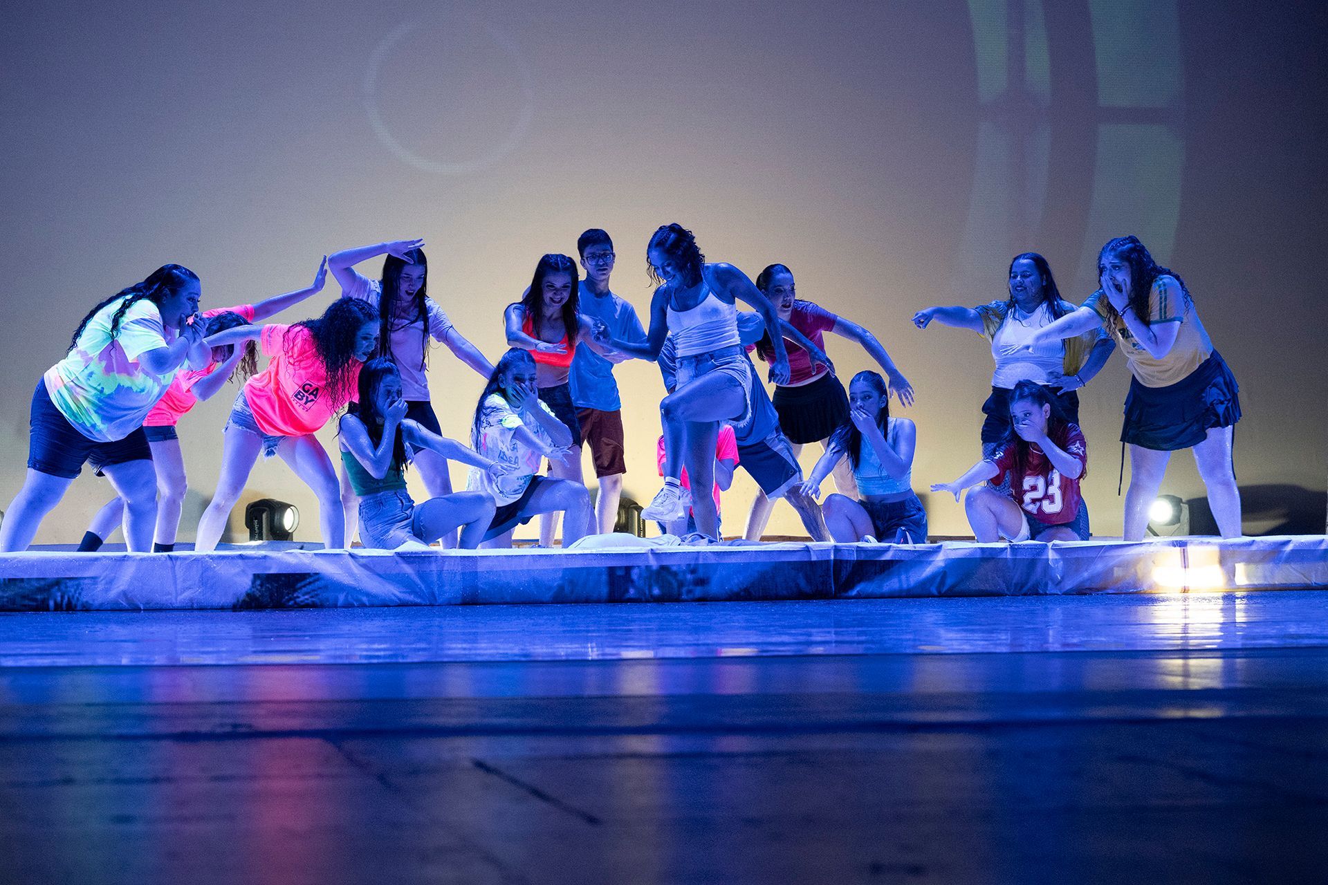 Bailarines con camisetas de neón actúan en un escenario con iluminación azul.