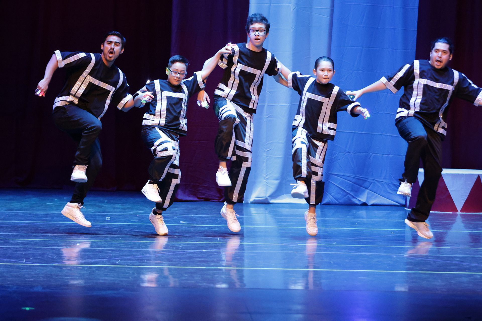 Cinco bailarines con trajes geométricos en blanco y negro saltando sobre un escenario.