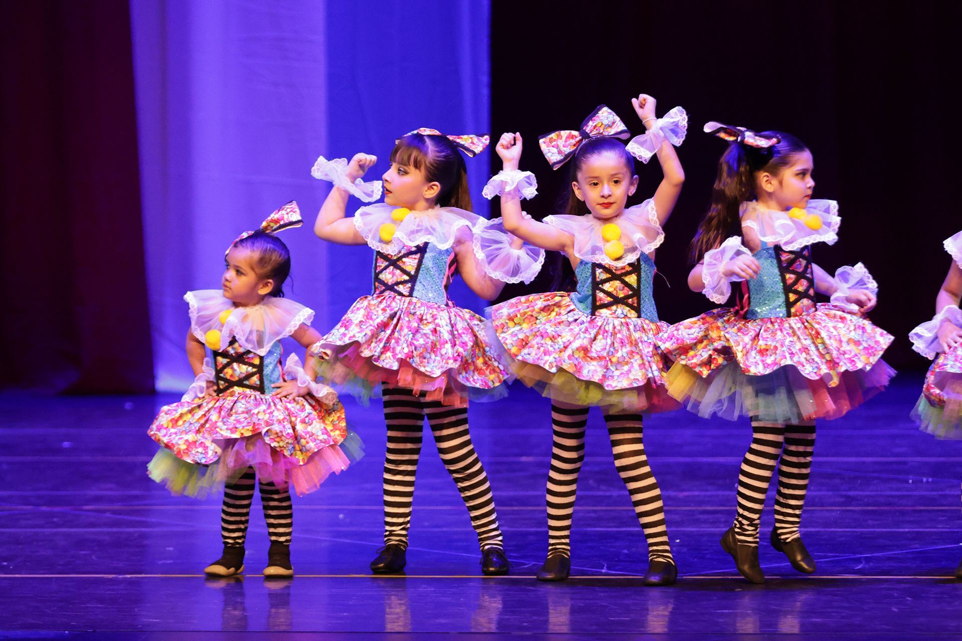 Cuatro jóvenes bailarines con coloridos trajes actúan en el escenario bajo luz azul.