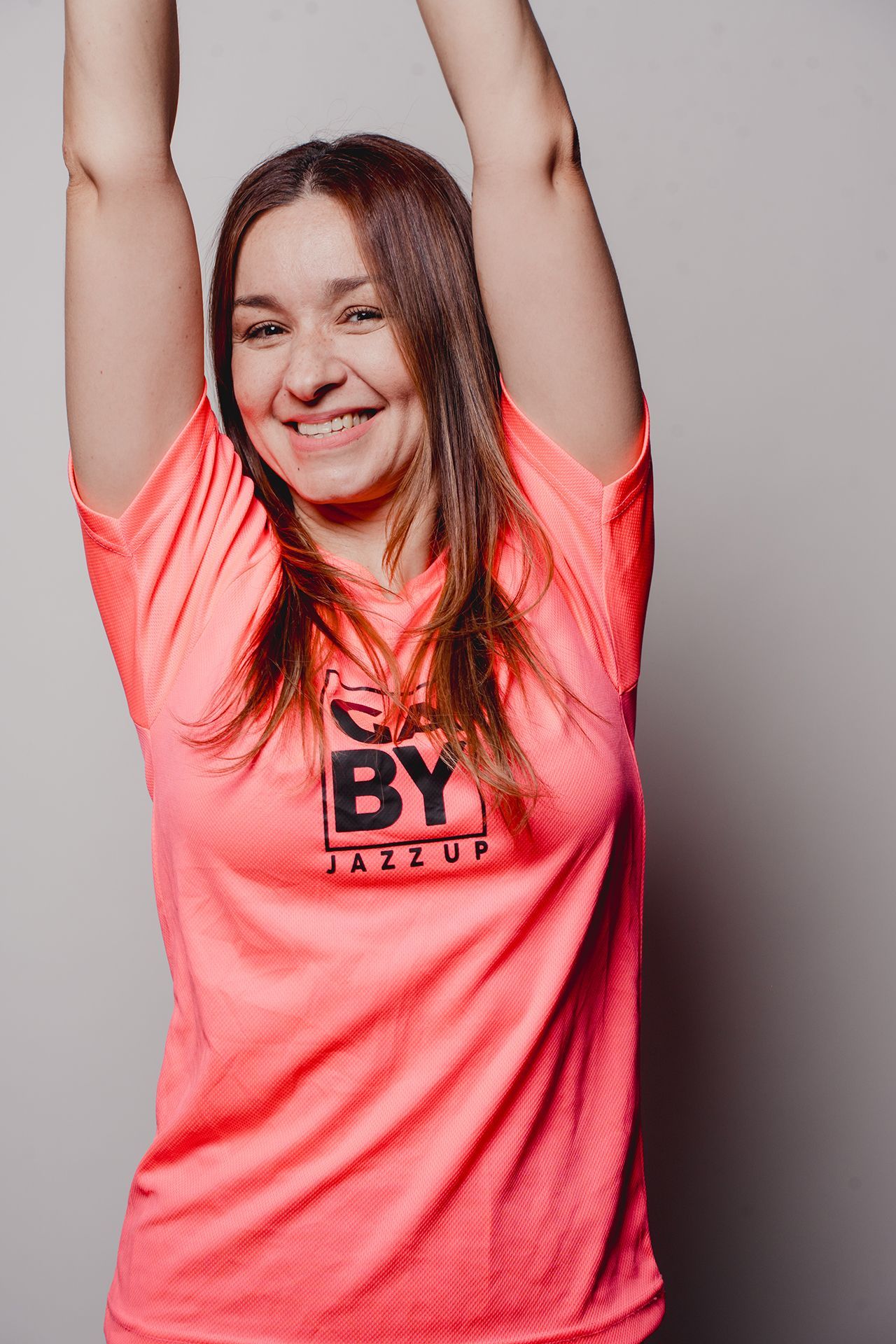 Mujer con una camiseta rosa neón, con los brazos levantados y sonriendo.