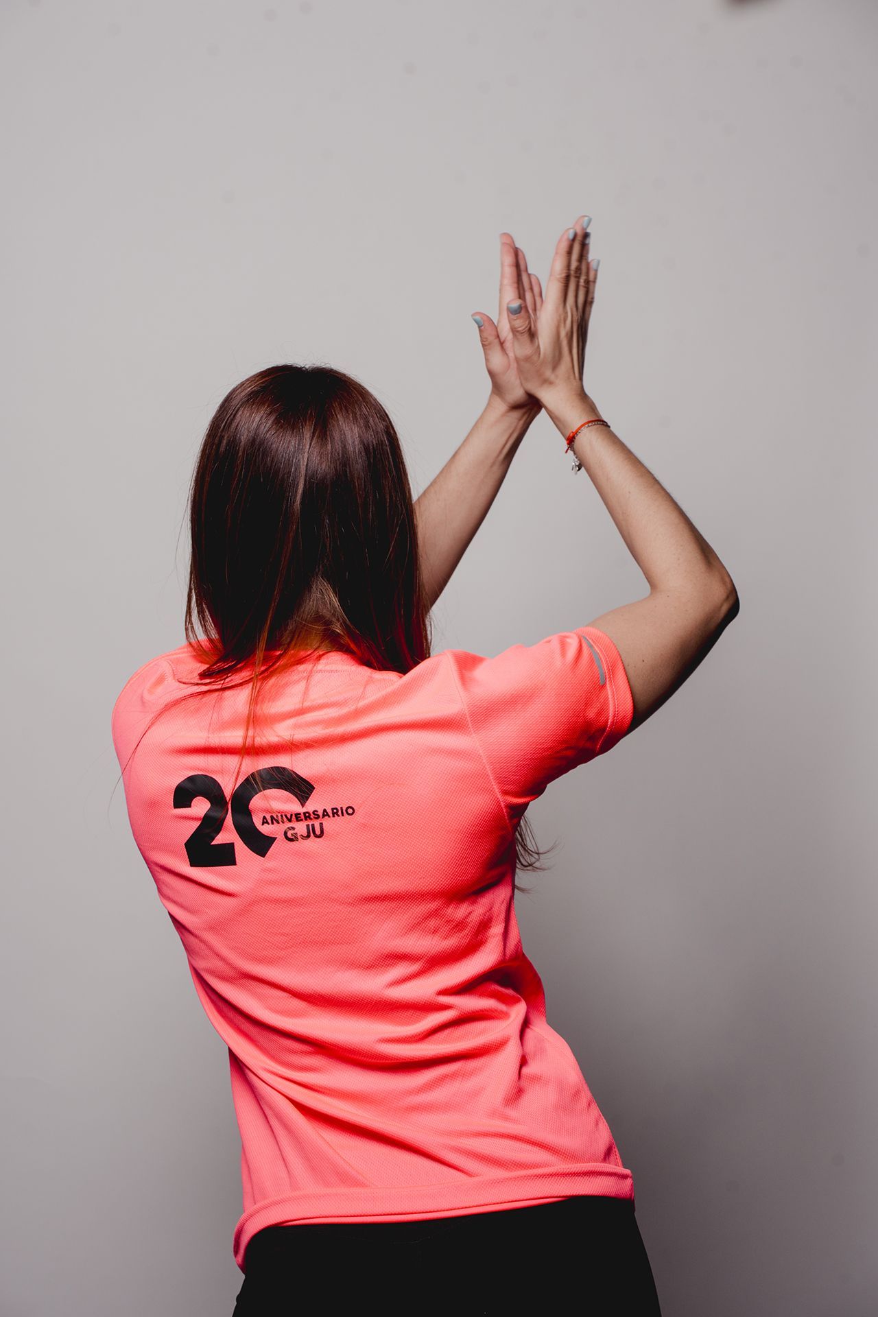 Mujer con camisa rosa aplaudiendo con las manos sobre la cabeza.