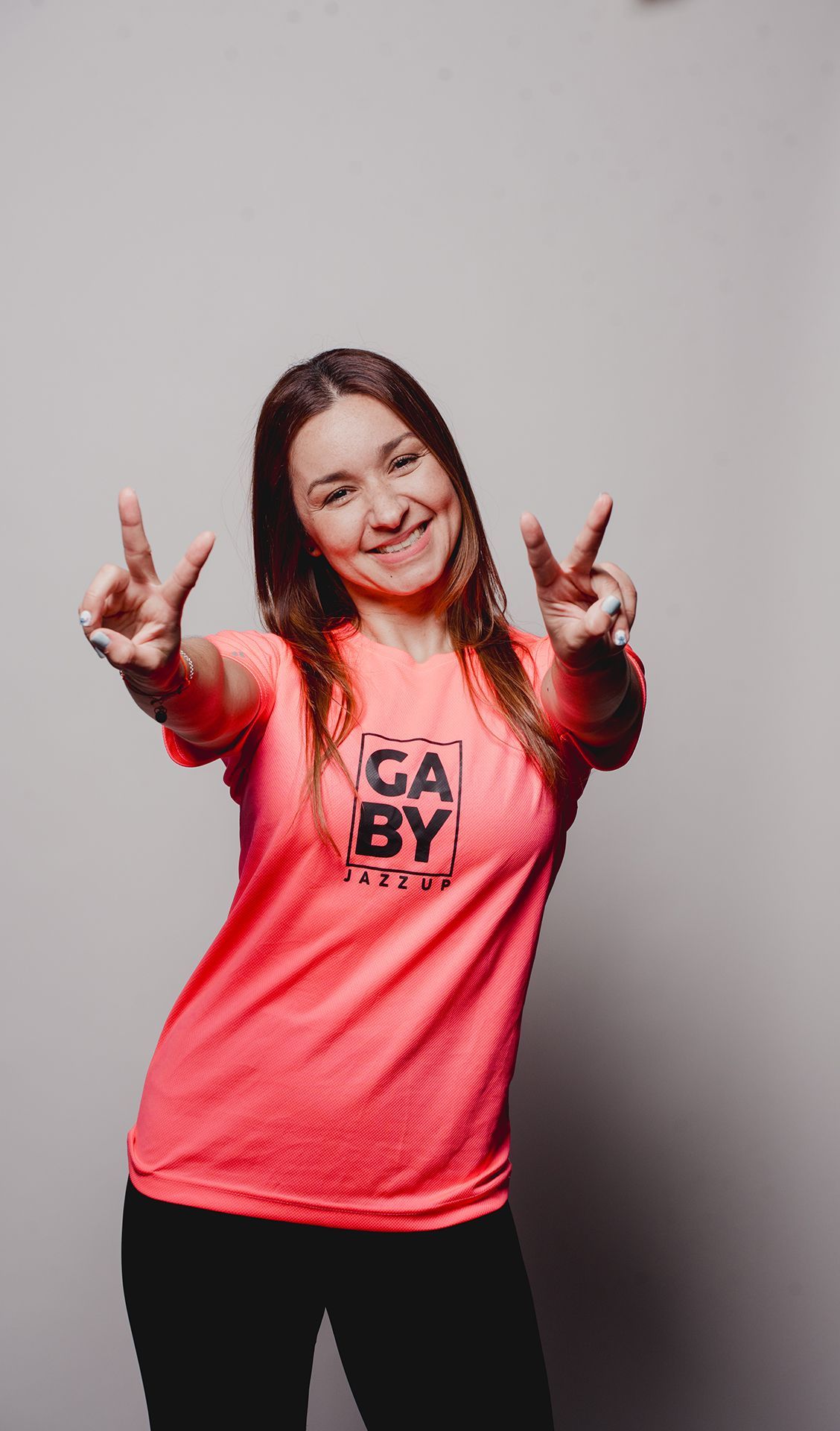 Mujer con camisa rosa haciendo la señal de la paz, sonriendo.