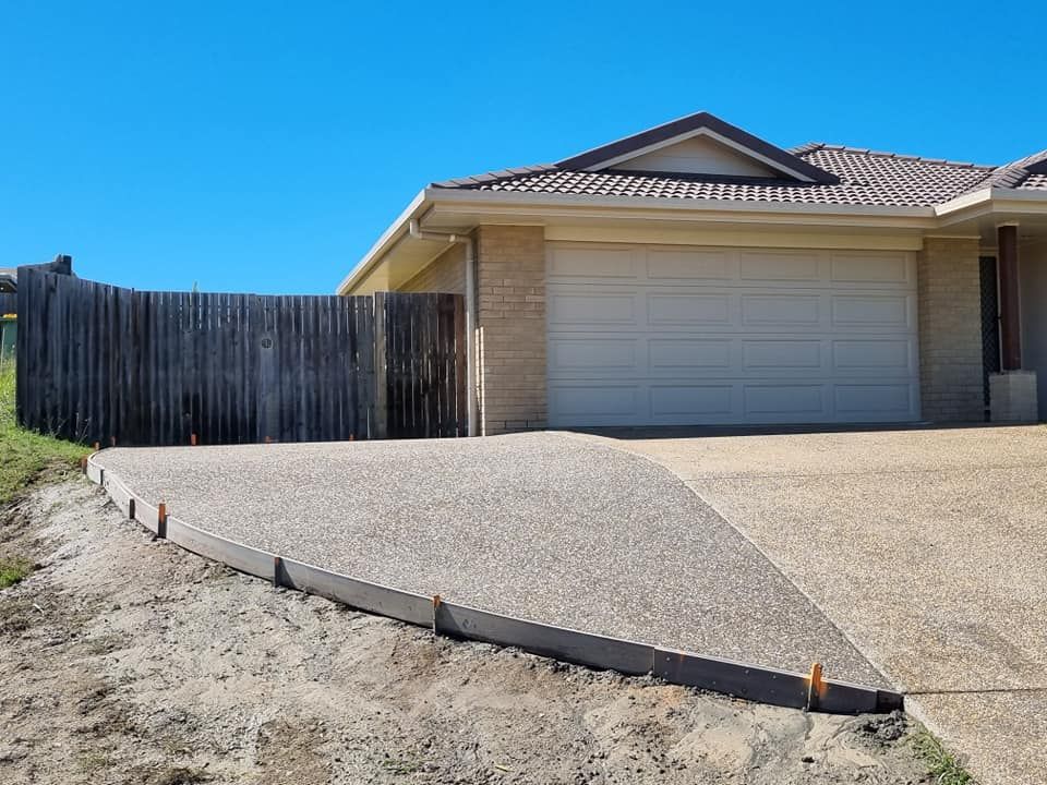 Concrete Driveway Leading to a House With a Garage and a Wooden Fence — SRS Concreting In Glenvale, QLD