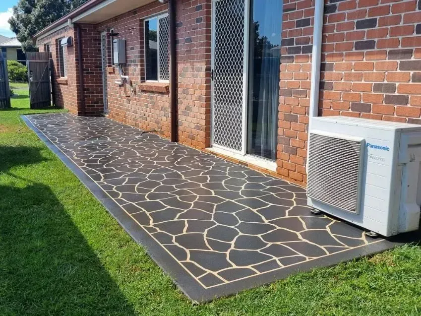 Brick Building With a Patterned Concrete Patio, Next to Green Grass and an Air Conditioner — SRS Concreting In Crows Nest, QLD
