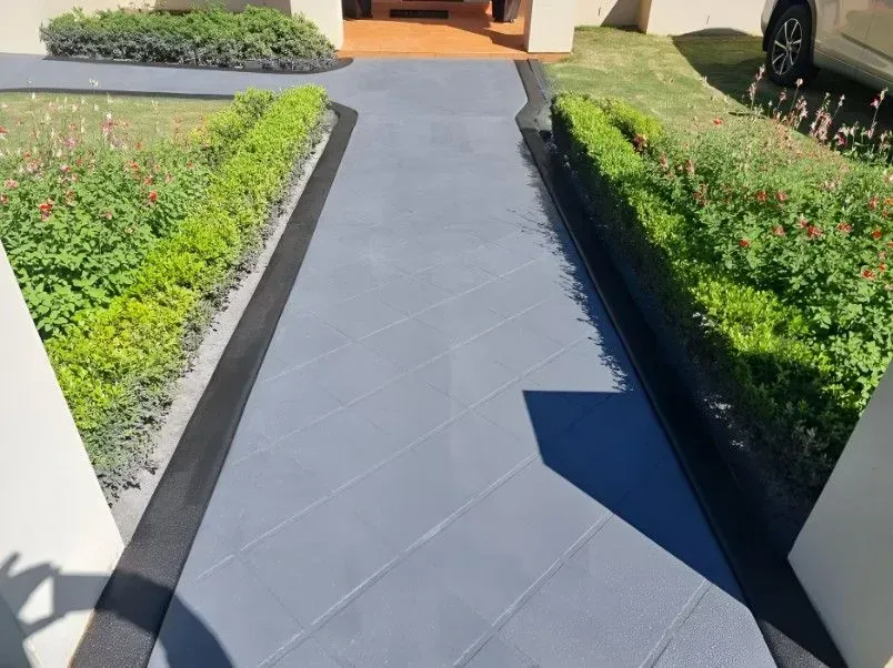 Grey Paved Walkway Lined With Green Bushes and Flowers Leading to a Home — SRS Concreting In Oakey, QLD