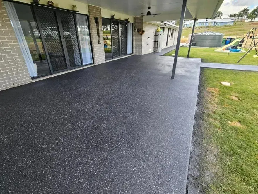 Black Speckled Concrete Patio Next to a Green Lawn and Sliding Glass Doors — SRS Concreting In Dalby, QLD
