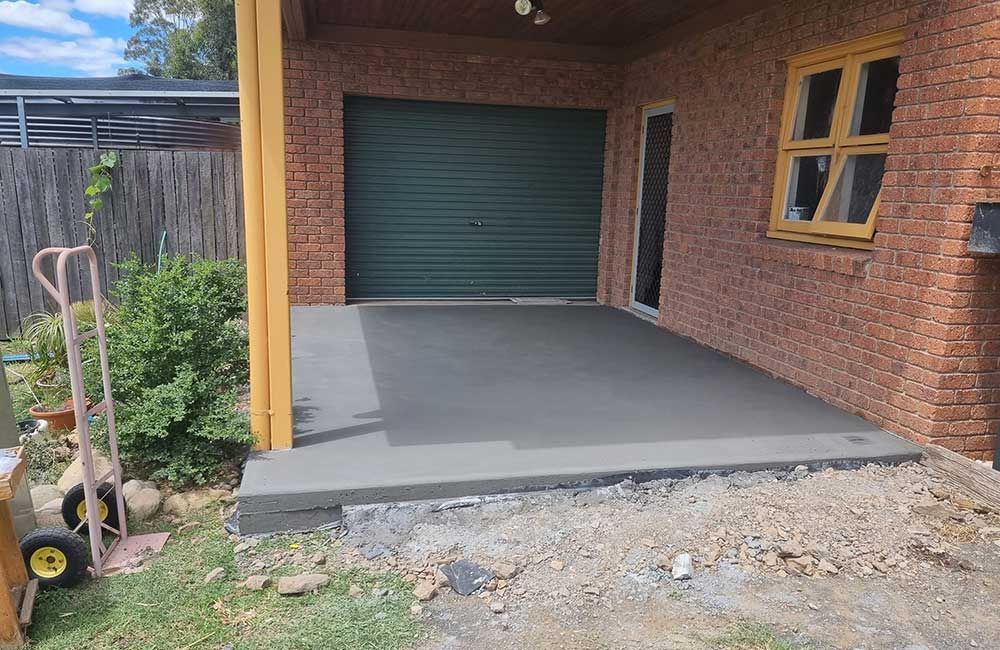 A New Concrete Patio With a Garage Door and Brick Building — SRS Concreting In Glenvale, QLD