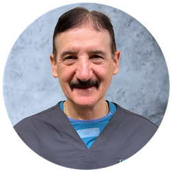 A man with a mustache is wearing a scrub top and smiling for the camera.