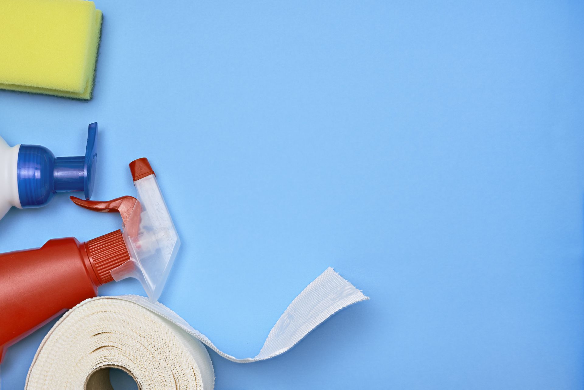 cleaning bottles, yellow sponge, paper towels laid on a bright blue background