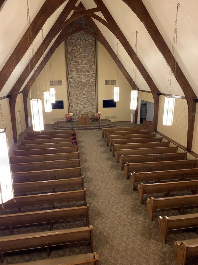 The inside of a church with rows of wooden benches and a stone fireplace.