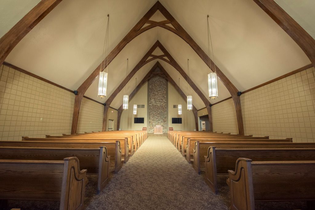 An empty church with wooden benches and a stone fireplace