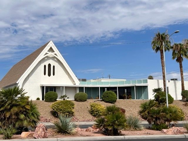 A white building with a triangle shaped roof and palm trees in front of it