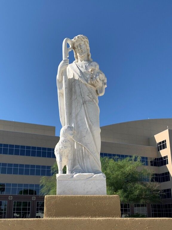 A statue of jesus holding a lamb in front of a building