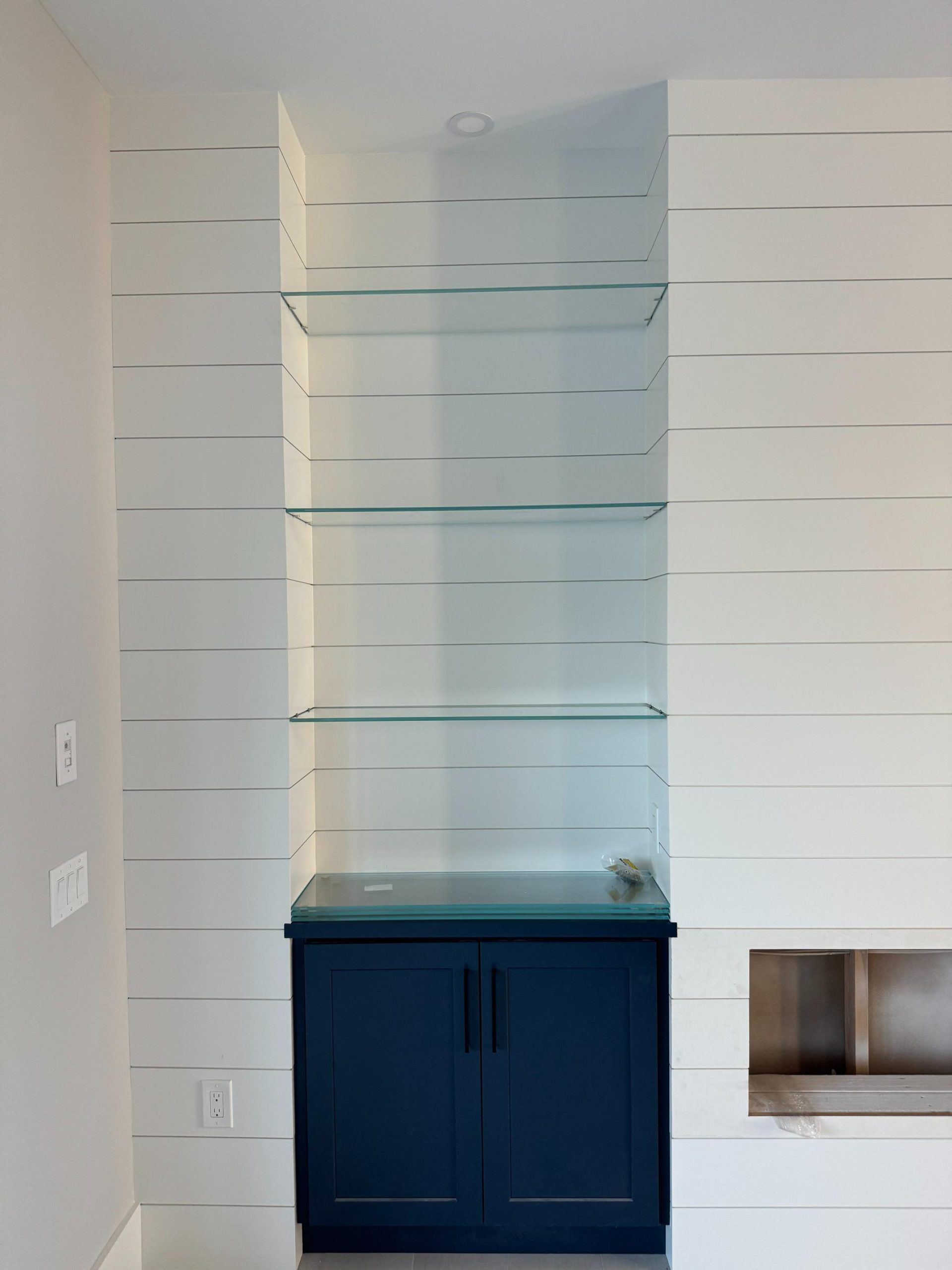 Built-in cabinet with glass shelves, painted blue, within a white wall niche.