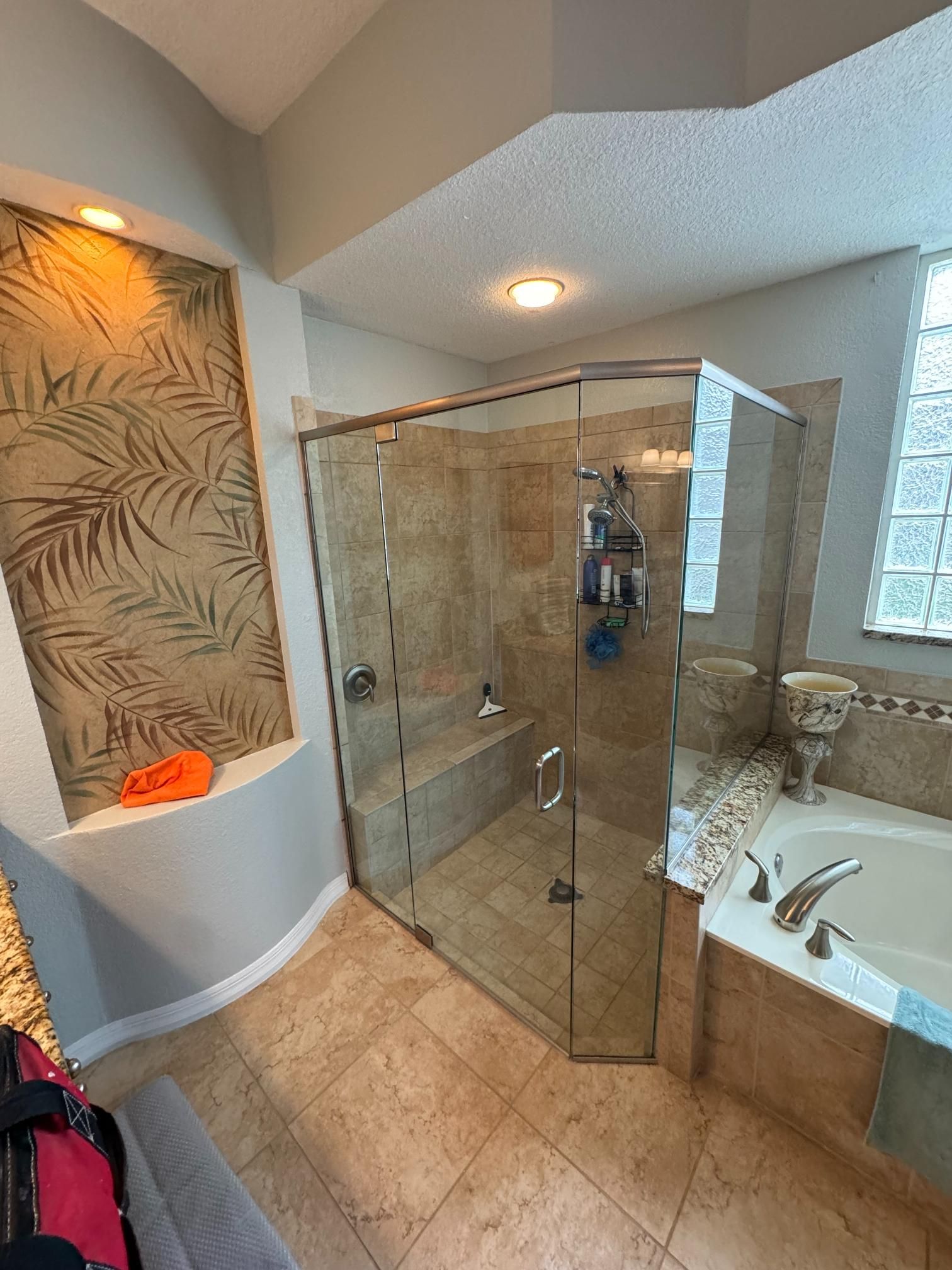 Bathroom with glass shower, tiled floor, built-in bench, and patterned wall.