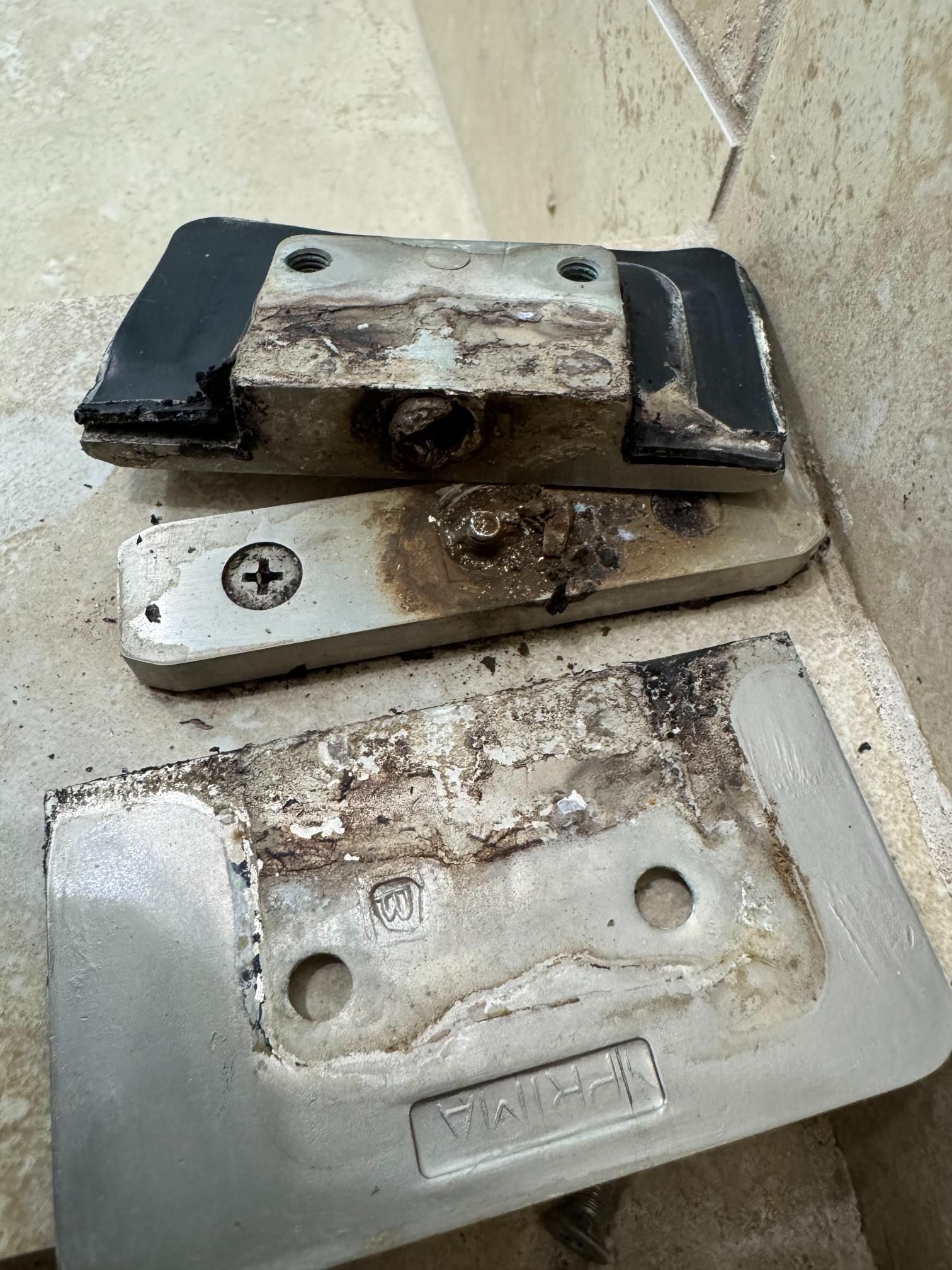 Three old metal door hinges covered in residue lie on a tile floor.