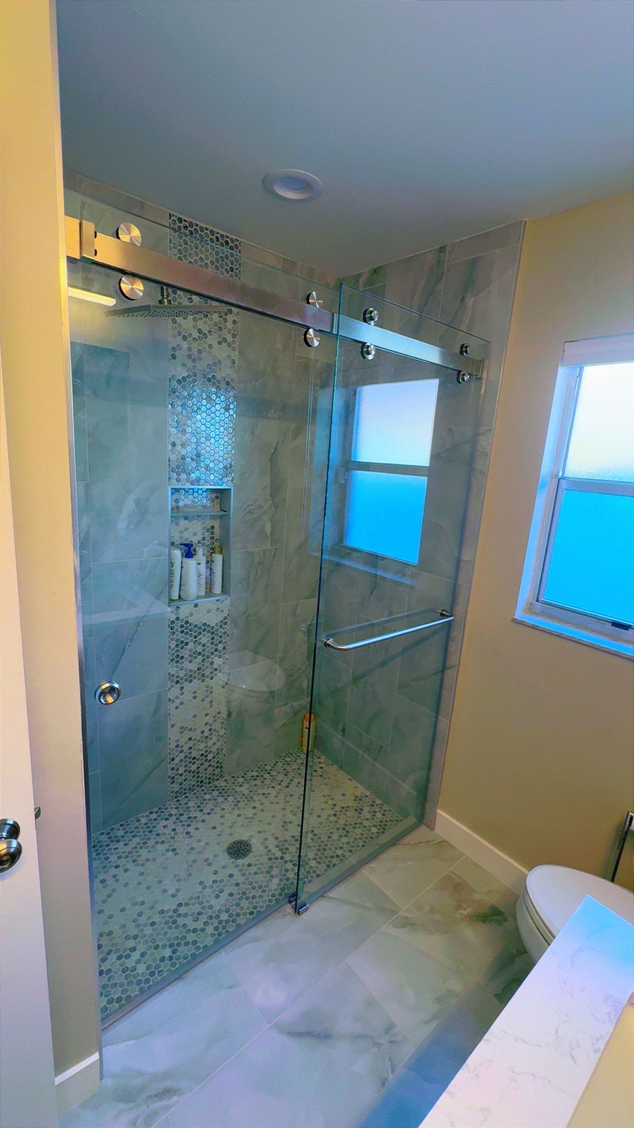 Glass shower with textured walls and sliding door, next to a window overlooking water.
