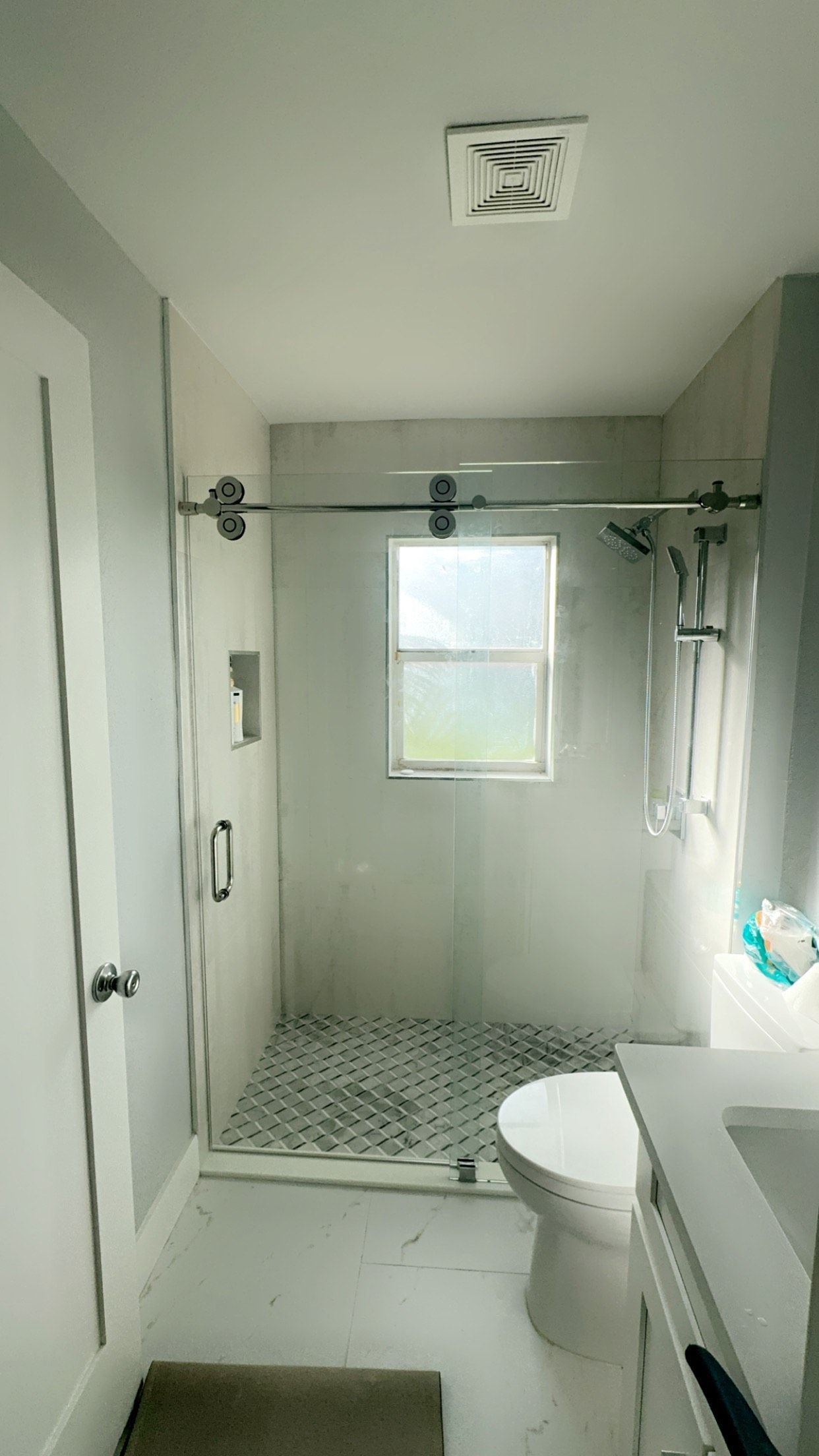 Bathroom with a glass shower, toilet, and a window. White and gray tones throughout.