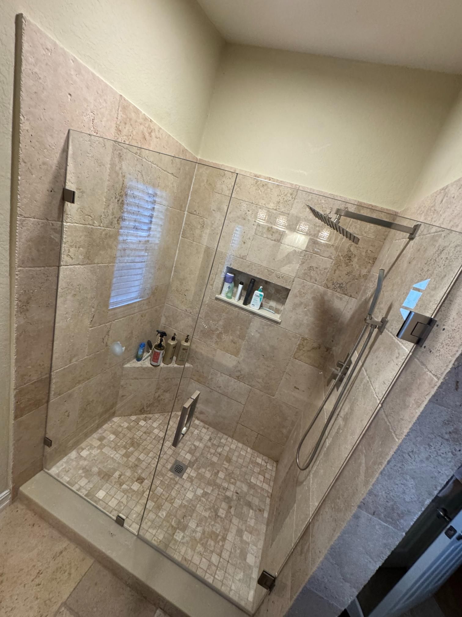 Corner shower with glass doors, stone tile walls and floor, and shower heads.
