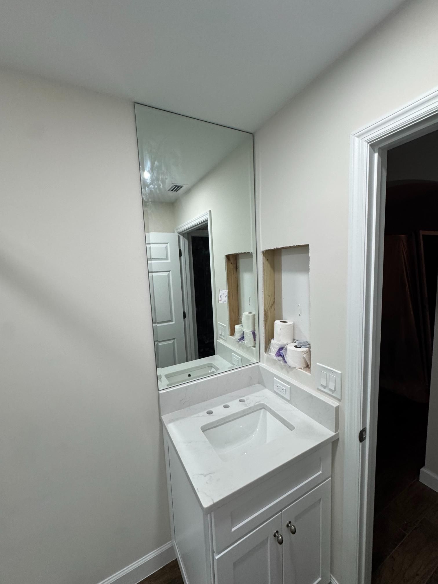 Bathroom with white vanity, large mirror, and recessed shelf with toilet paper.