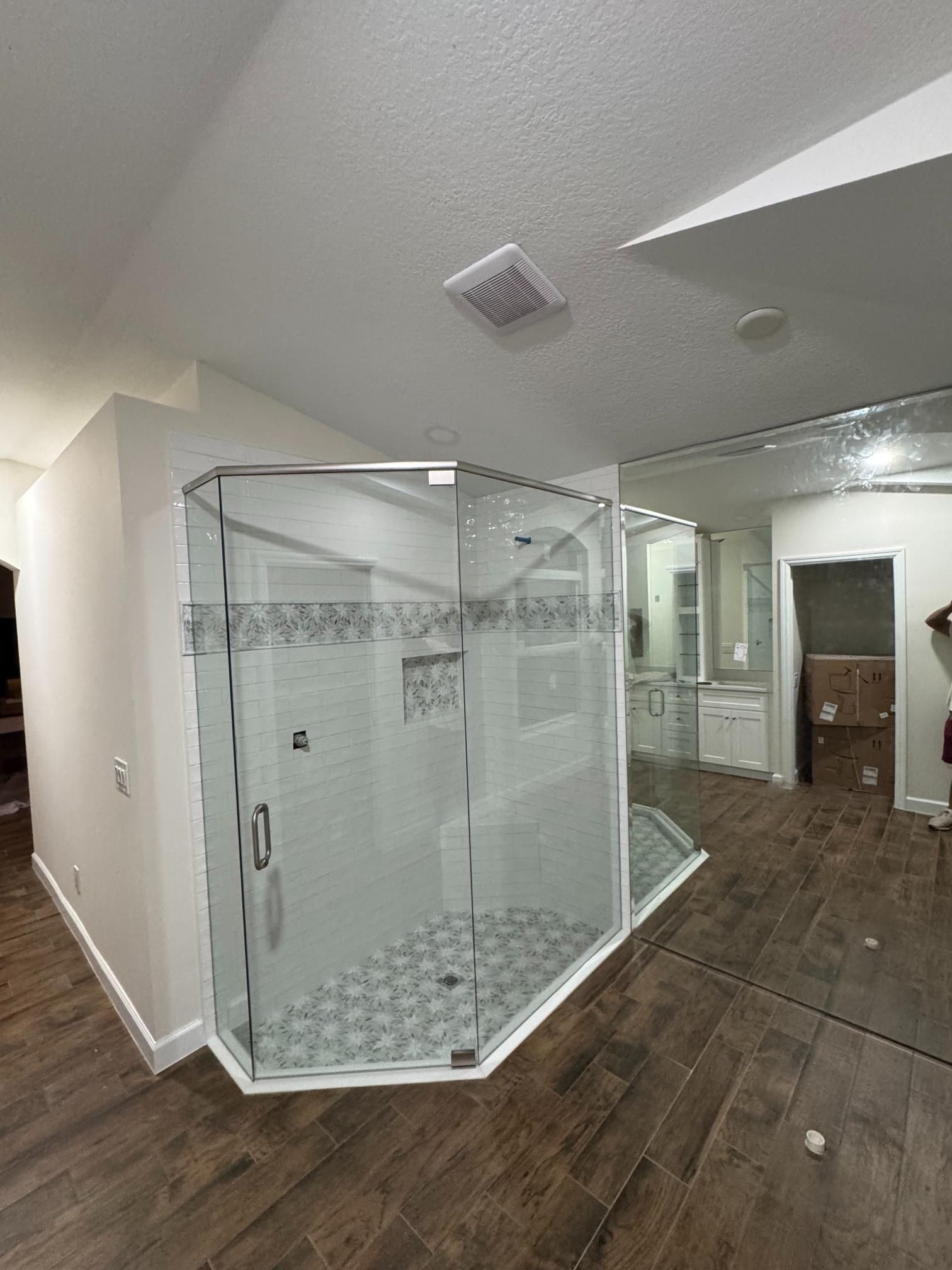 Bathroom with a glass-enclosed shower, white tile, and dark wood-look flooring.
