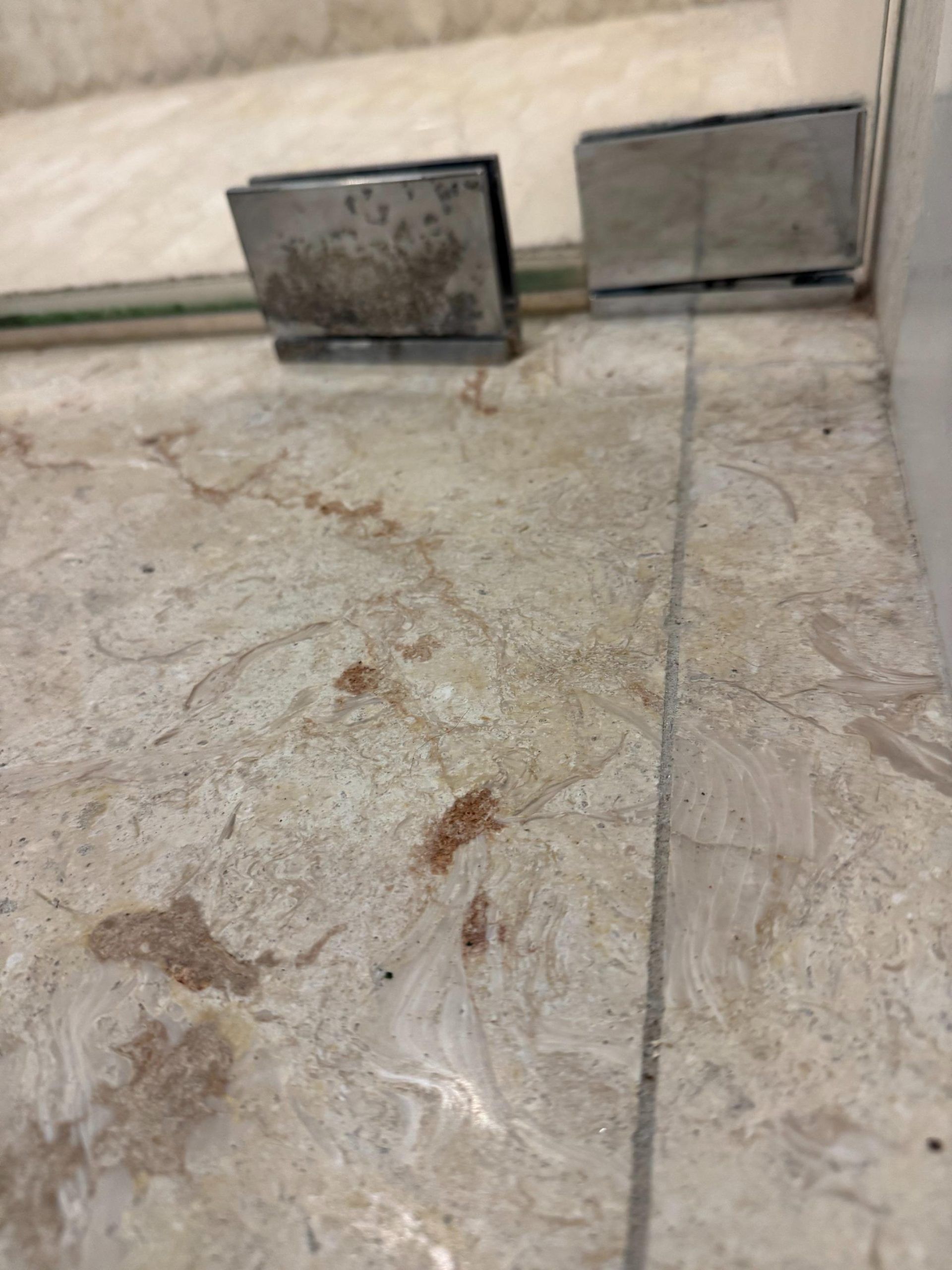 Marble floor with shower door hinges and reddish stains.