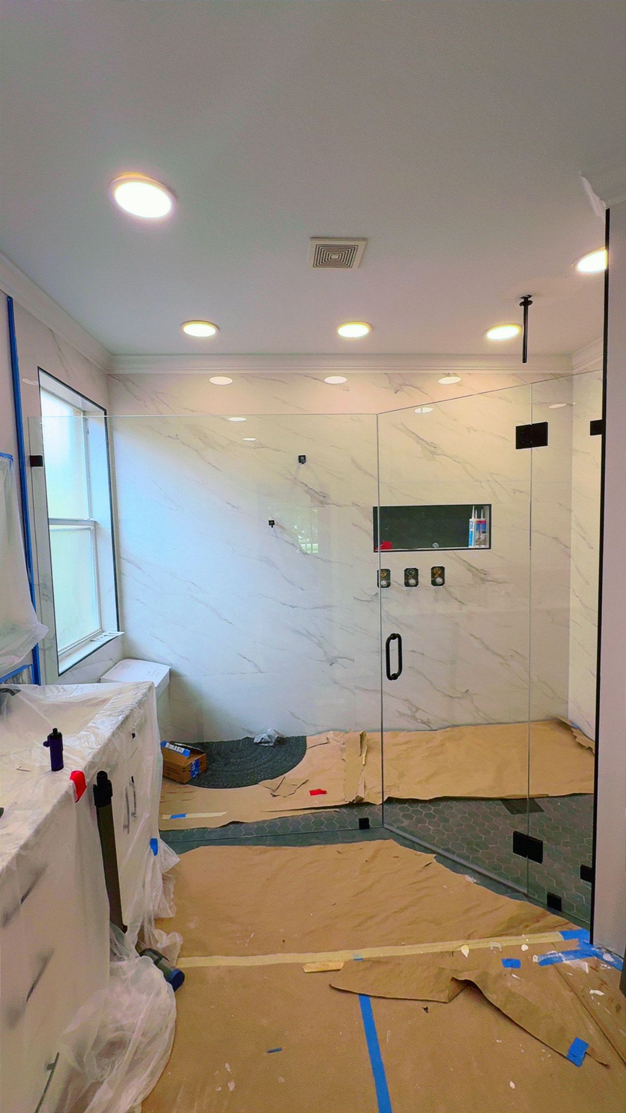 Bathroom under construction, white marble tile, shower enclosure, cardboard floor protection.