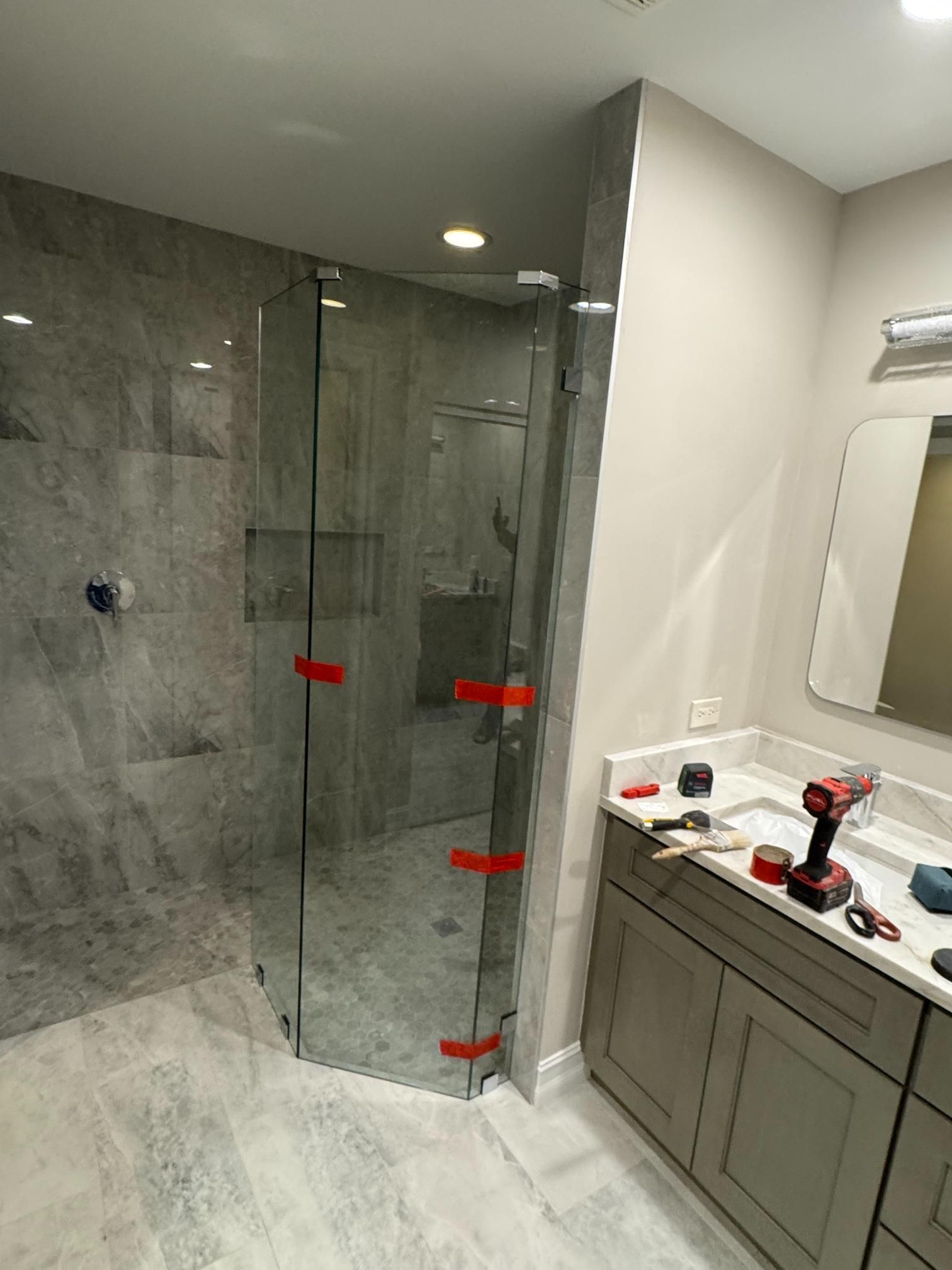 New shower installation in a bathroom with glass doors and tile walls. A vanity with a mirror and tools are visible.