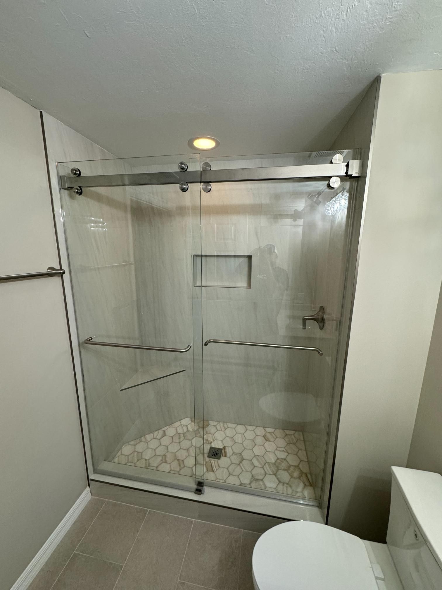Bathroom with glass sliding shower door, white toilet, and gray tiled floor and walls.