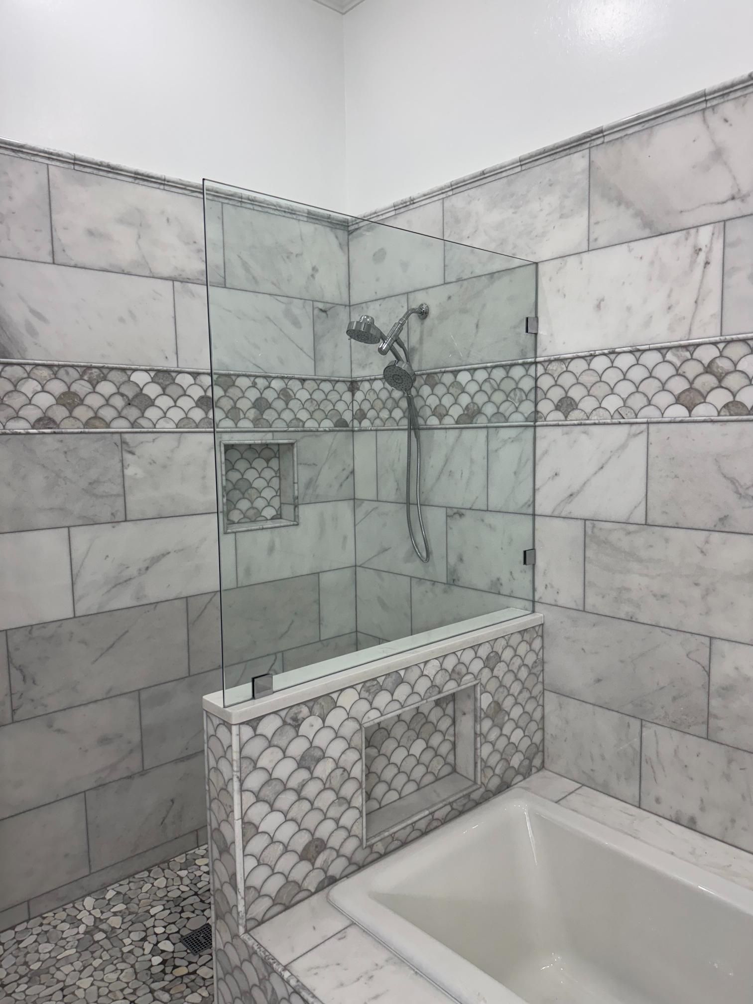 Marble-tiled shower enclosure with glass doors, a built-in shelf, and a shower head.