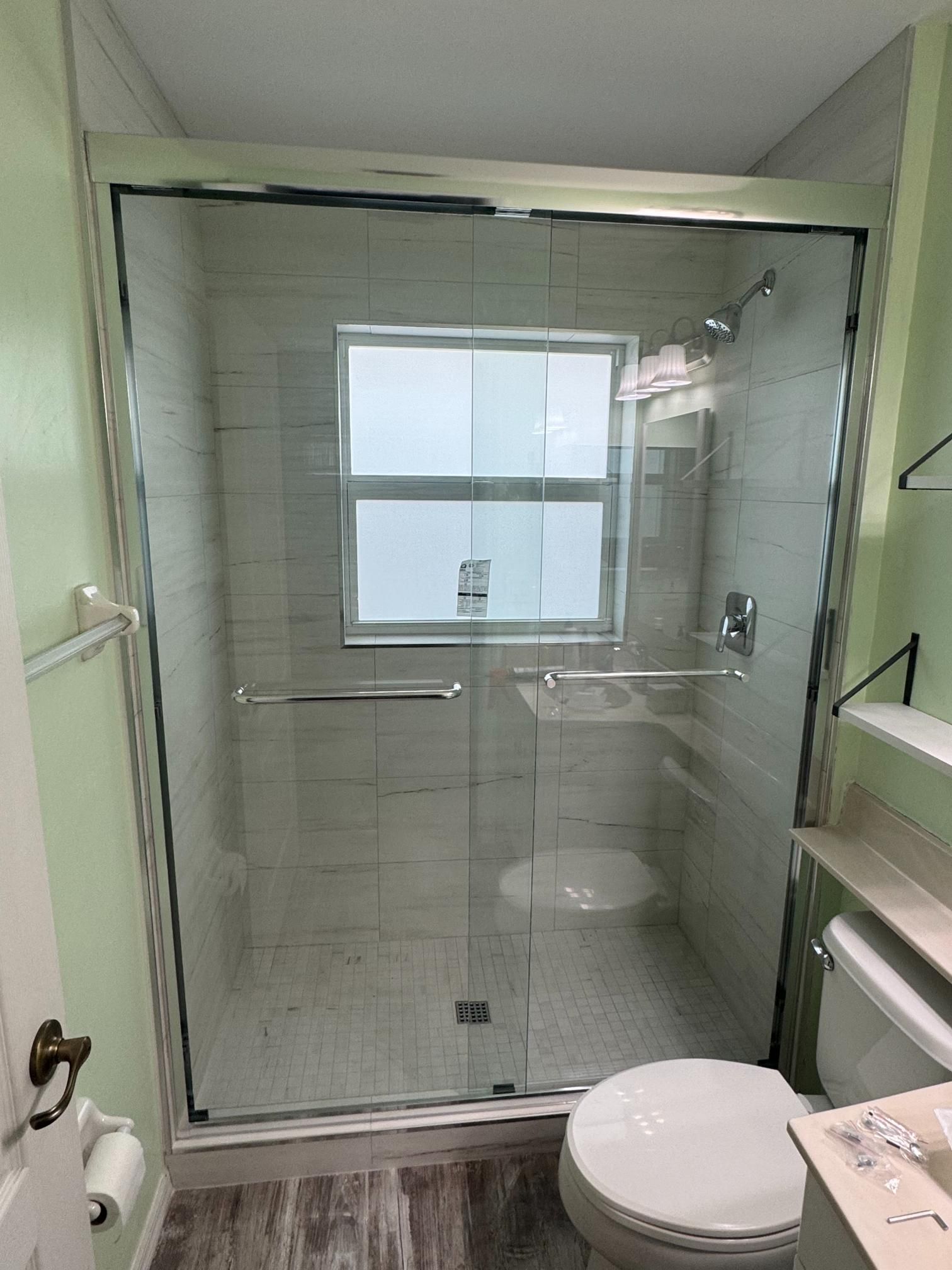 Shower with glass doors, white tiled walls, window, and chrome fixtures.
