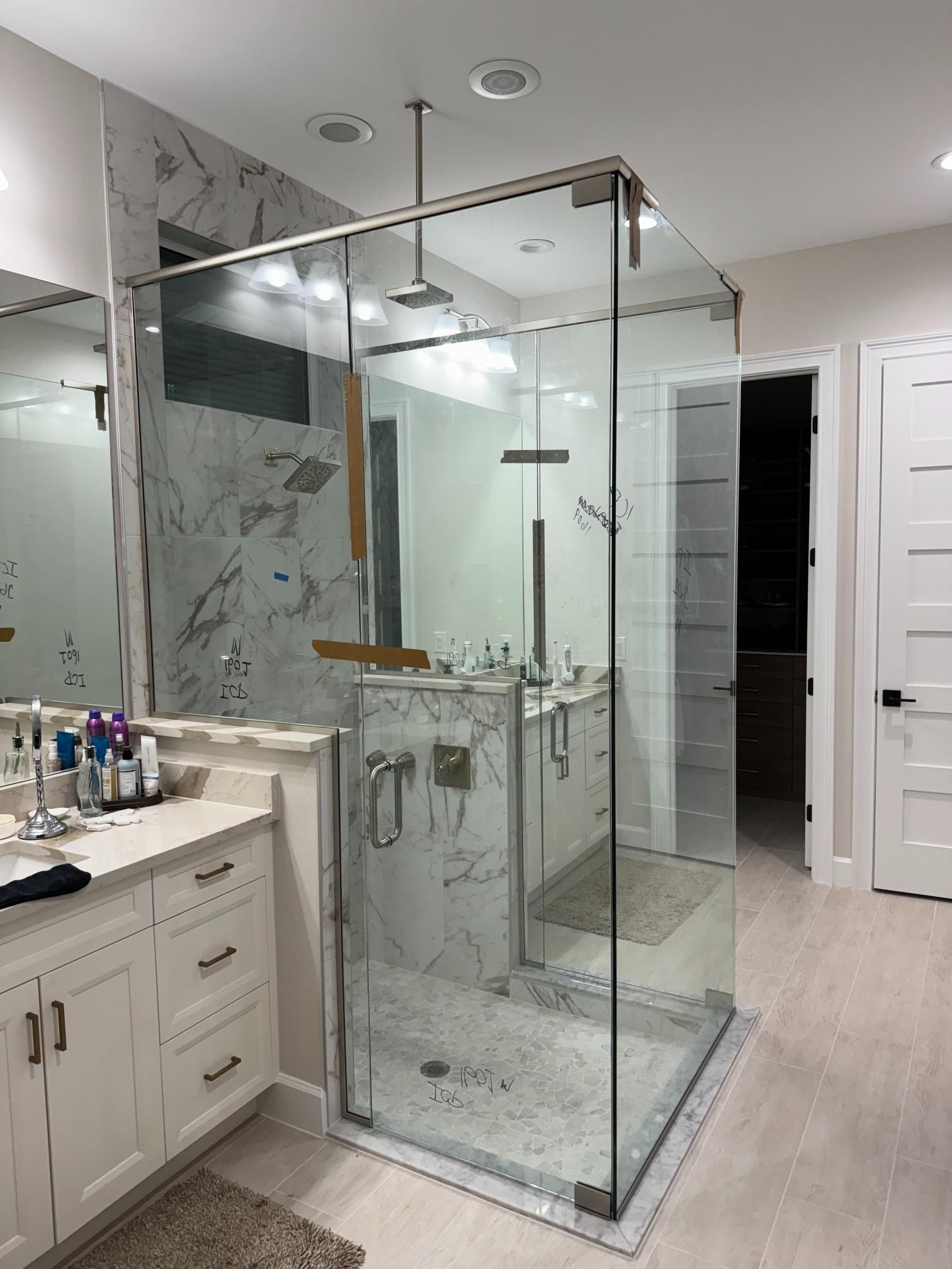 Modern bathroom with large glass shower enclosure. White cabinets, marble backsplash, and light wood-look flooring.