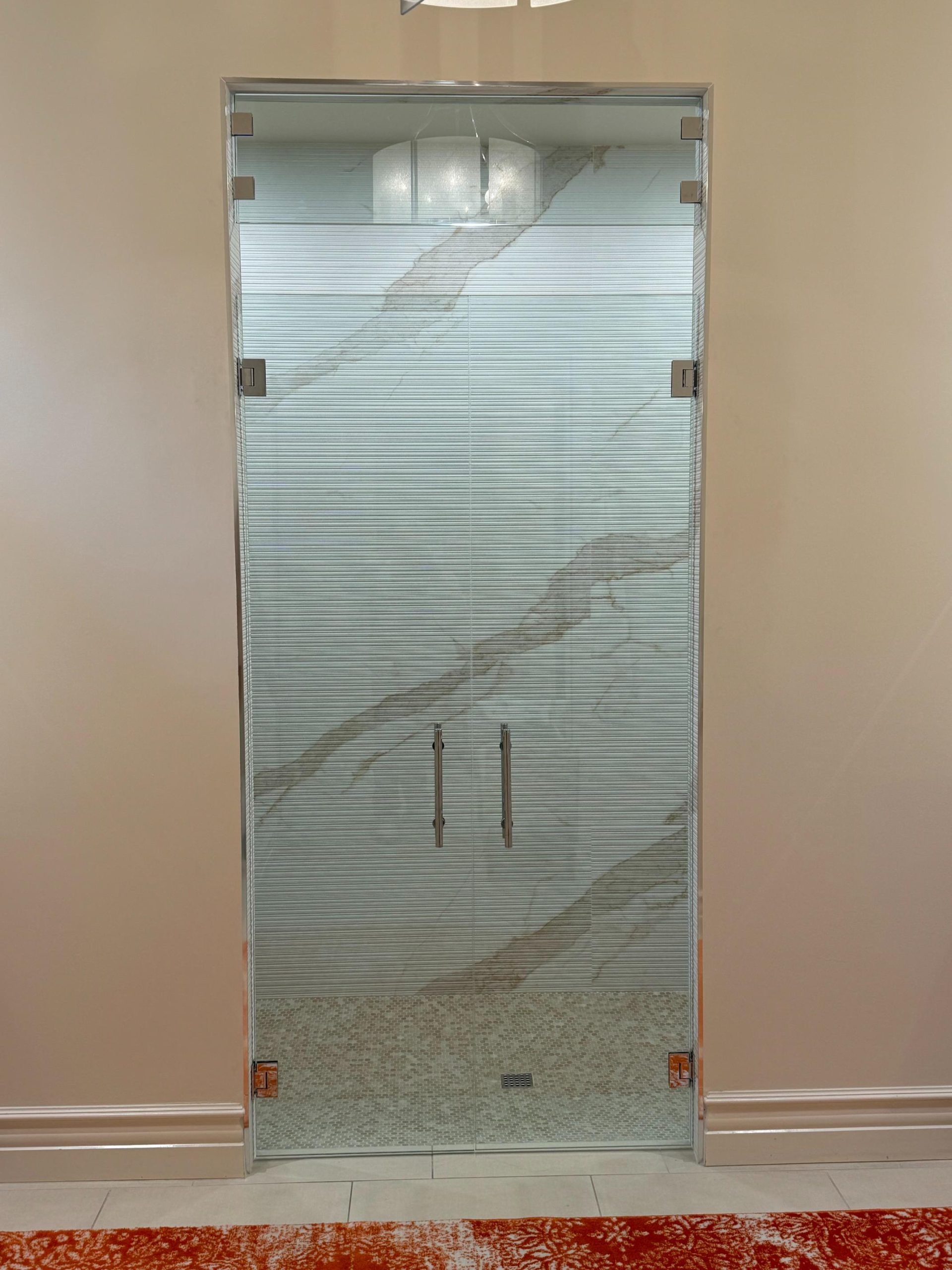 Glass shower door with a rippled texture. Chrome handles and hinges. Beige walls, red carpet.