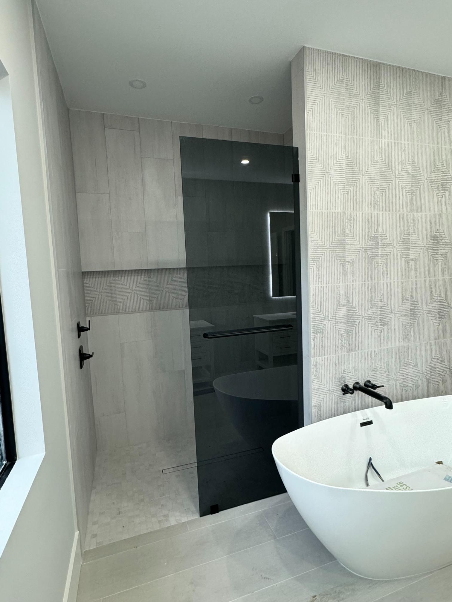 Modern bathroom with a glass shower door, a white bathtub, and gray and white patterned tiles.