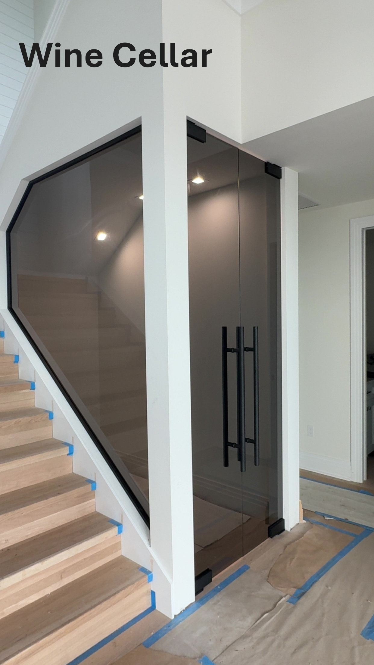 Wine cellar entrance with glass door and black handles, next to staircase.