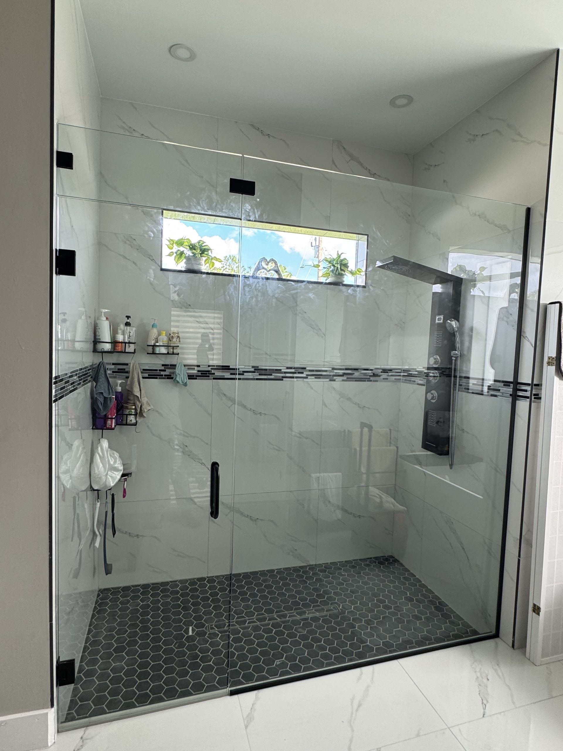 Modern shower with glass walls, black trim, and black and white patterned tile.