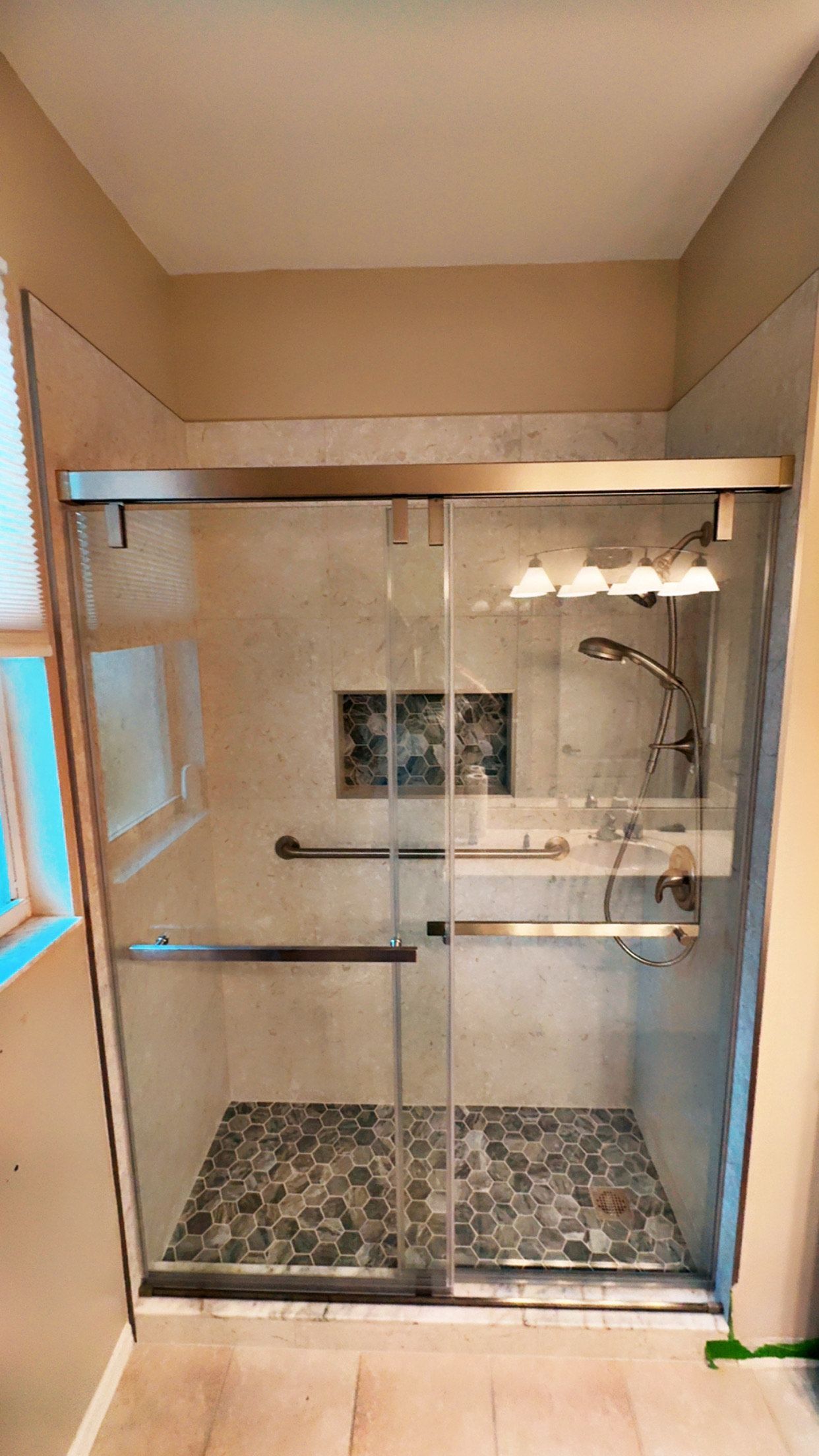 Shower stall with sliding glass doors, stone tile floor and walls.