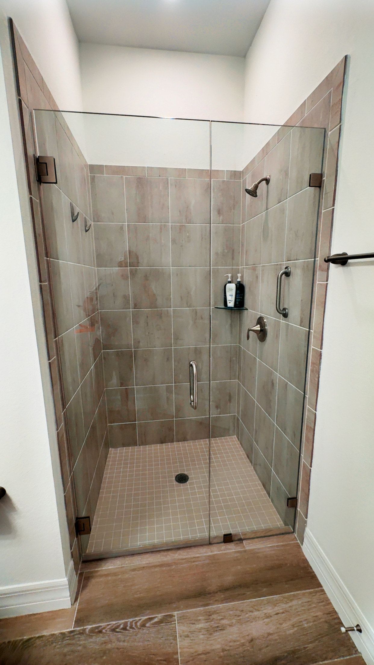 Shower with glass doors and tiled walls; beige and brown tones.