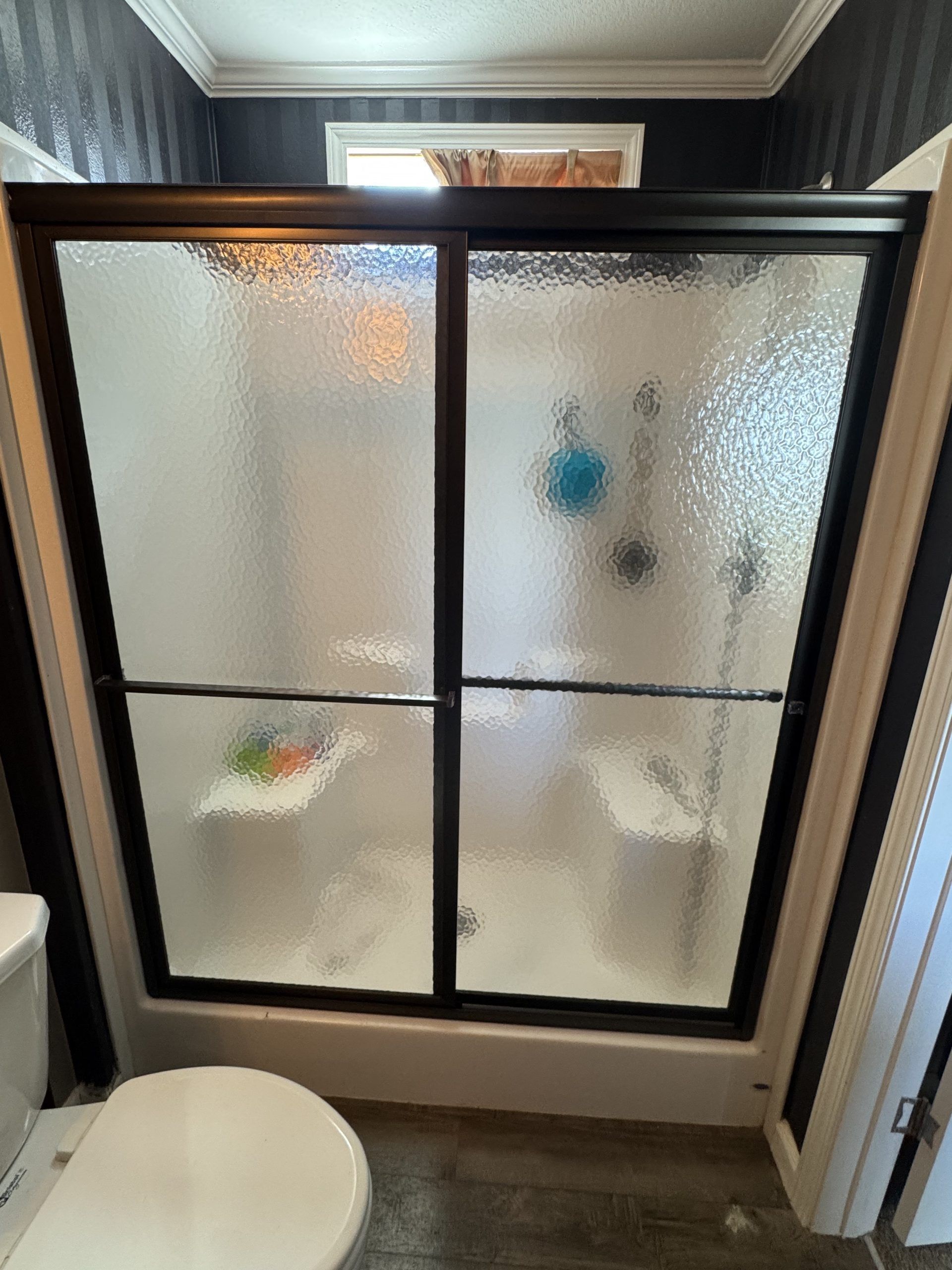 A frosted-glass shower door with a dark frame in a bathroom. A toilet is in the foreground.