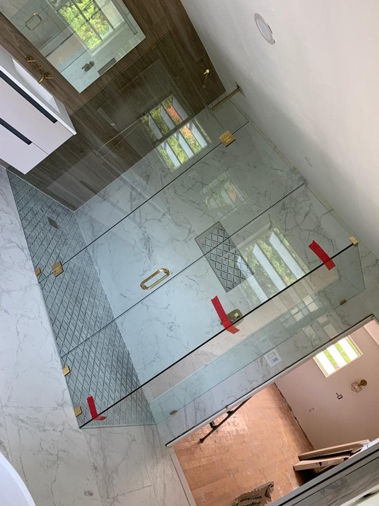 Glass shower enclosure with gold hardware in a bathroom.