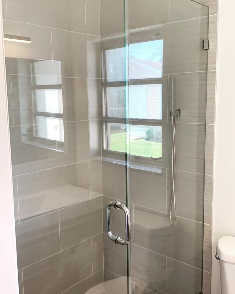 Glass shower with gray tiled walls, window, and chrome hardware.