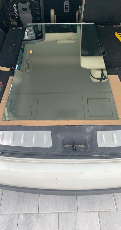 Large rectangular mirror resting in the open trunk of a light-colored vehicle, on cardboard.