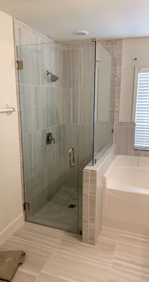 Glass shower enclosure with gray tile walls and a white bathtub.