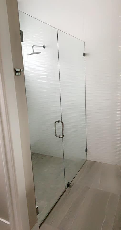 Glass shower enclosure with black hardware, white subway tile, and grey floor.