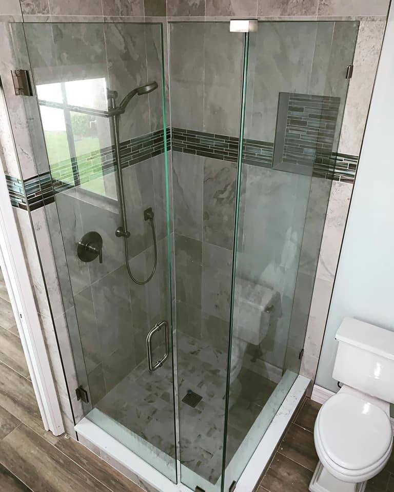 Glass shower stall in a bathroom with gray tile, toilet, and wooden floor.