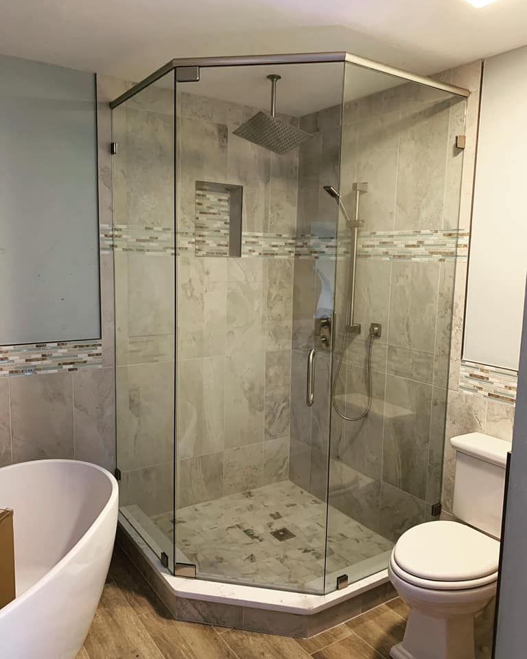 Glass-enclosed corner shower with gray tile, showerhead, and a toilet. Bathtub on the left.