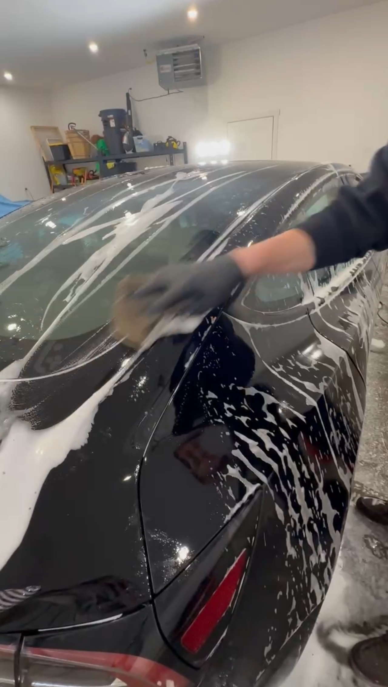 A person is washing a black car in a garage.